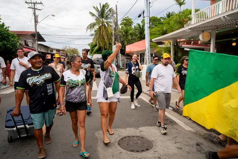 Fans in Bocas jerseys walking down a street in Bocas Town with the green and yellow Bocas flag