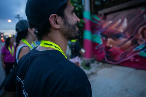 A man admiring a mural with a neon Too Much Tours lanyard
