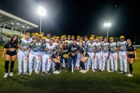 The Bocas baseball team posing on the field at night with fans and dancers